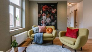Et værelse med to lænestole, en radiator, et vindue og et stort blomstermotiv på væggen.
