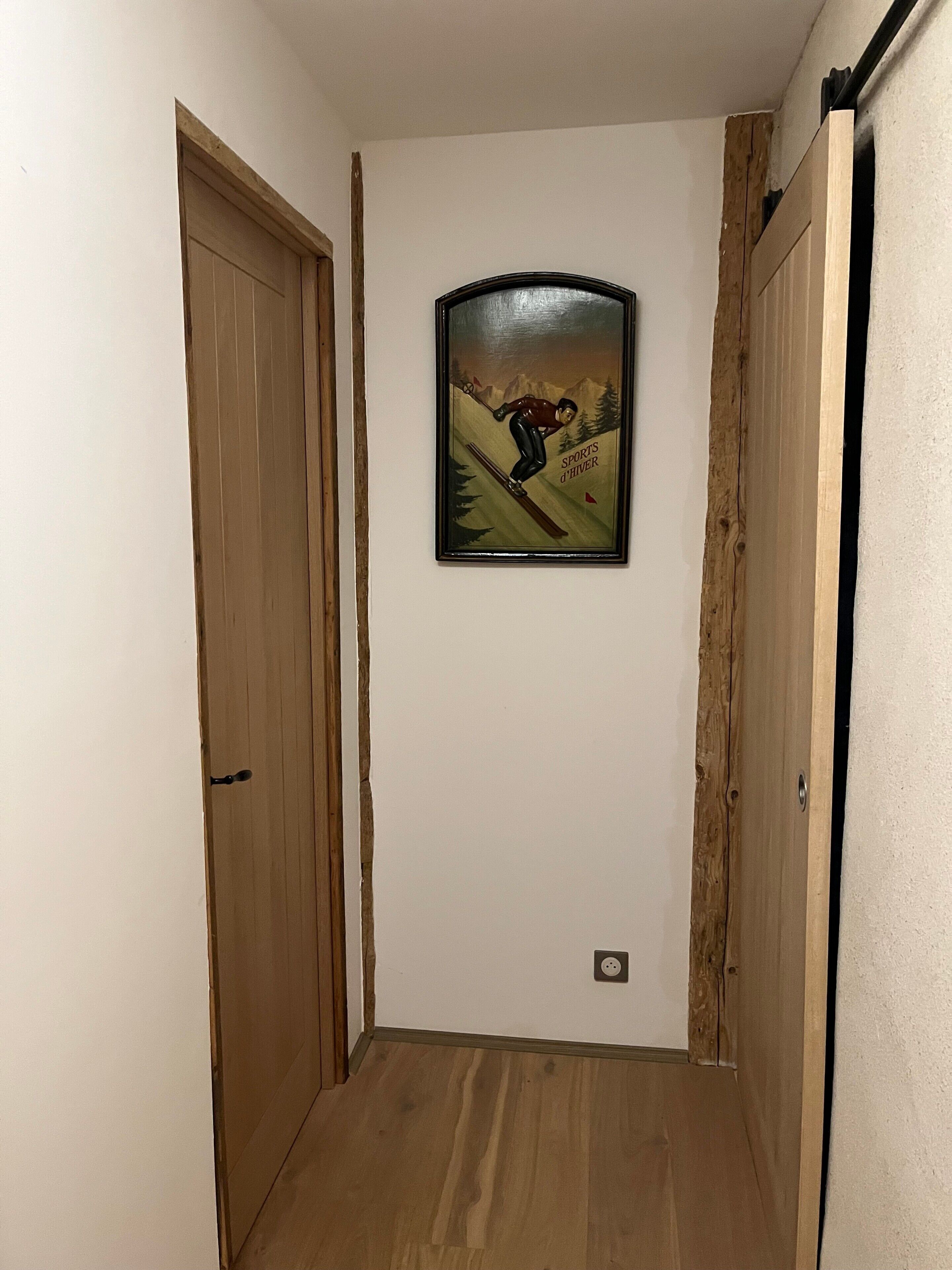 A narrow hallway with wooden doors and a framed picture on the wall.