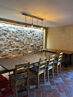 A dining area with a stone wall, wooden table, and chairs. - Holiday Home 'Gite Les 4 Saisons' with Mountain View, Private Terrace and Wi-Fi (Val de Chaise)