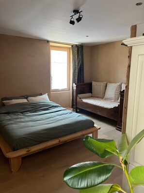 A bedroom with a wooden bed, a smaller bed, a window, and a plant. - Holiday Home 'Gite Les 4 Saisons' with Mountain View, Private Terrace and Wi-Fi (Val de Chaise)