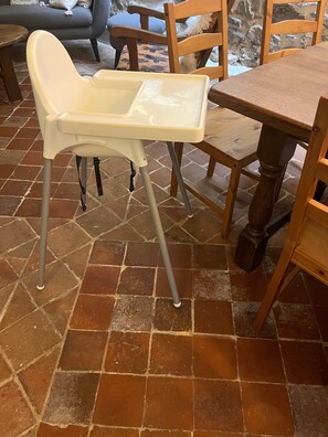 A dining area with a high chair, wooden chairs, a table, and a stone-tiled floor. - Holiday Home 'Gite Les 4 Saisons' with Mountain View, Private Terrace and Wi-Fi (Val de Chaise)