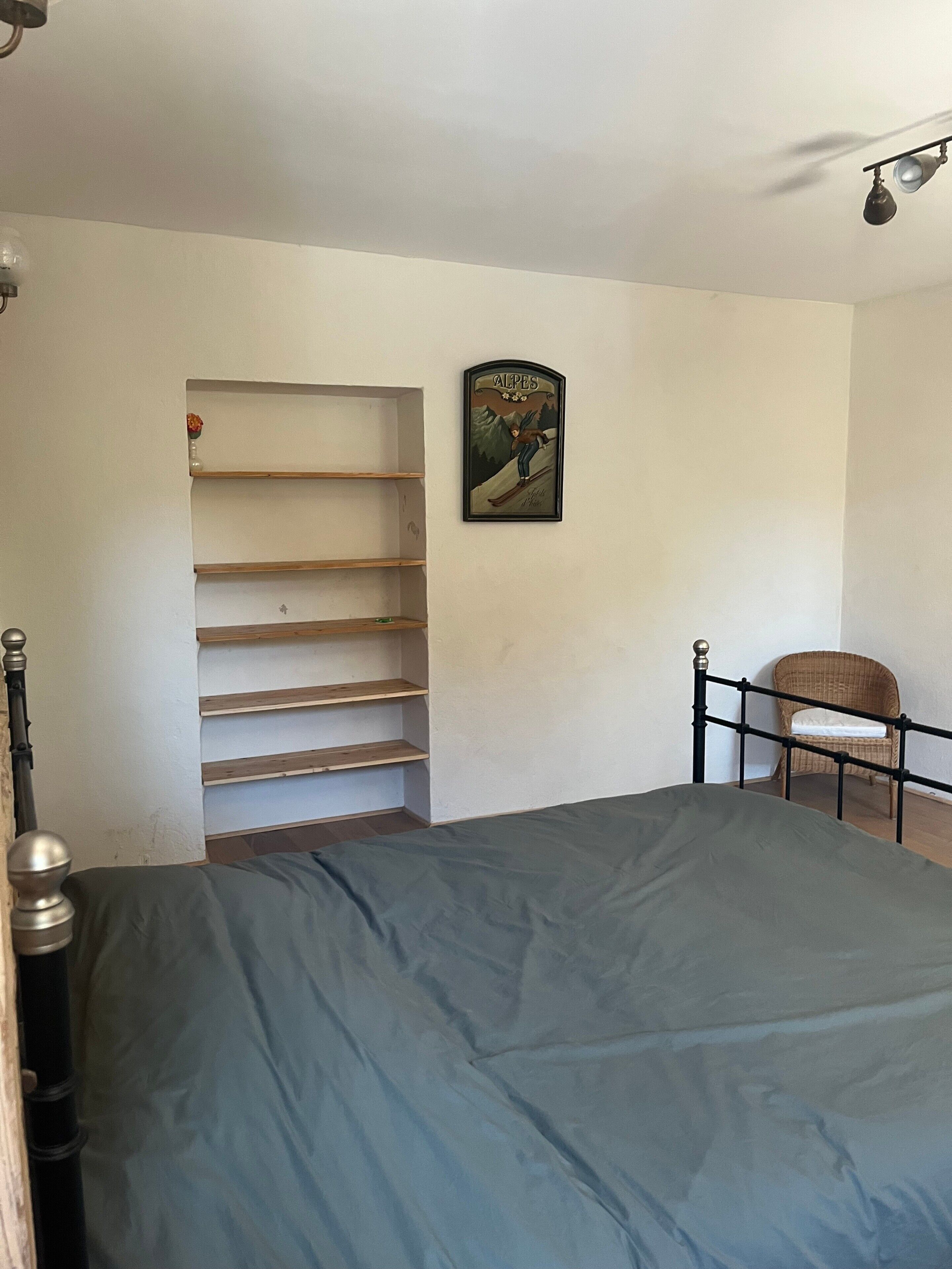 A bedroom with a bed, a chair, a shelf unit, and a poster on the wall.