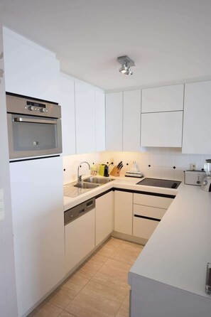 A modern kitchen with white cabinetry, a built-in oven, a sink, and a countertop with a toaster and a blender. - Waterfront promenade apt w/ beach access (Middelkerke)