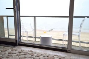 A room with a large glass door leading to a beach view, a round table with a glass, and two clear chairs. - Waterfront promenade apt w/ beach access (Middelkerke)