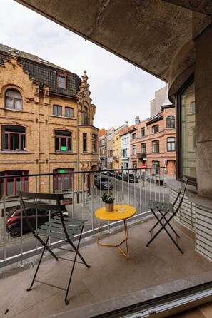 Un balcón con dos sillas y una pequeña mesa, con vista a una calle con edificios históricos.