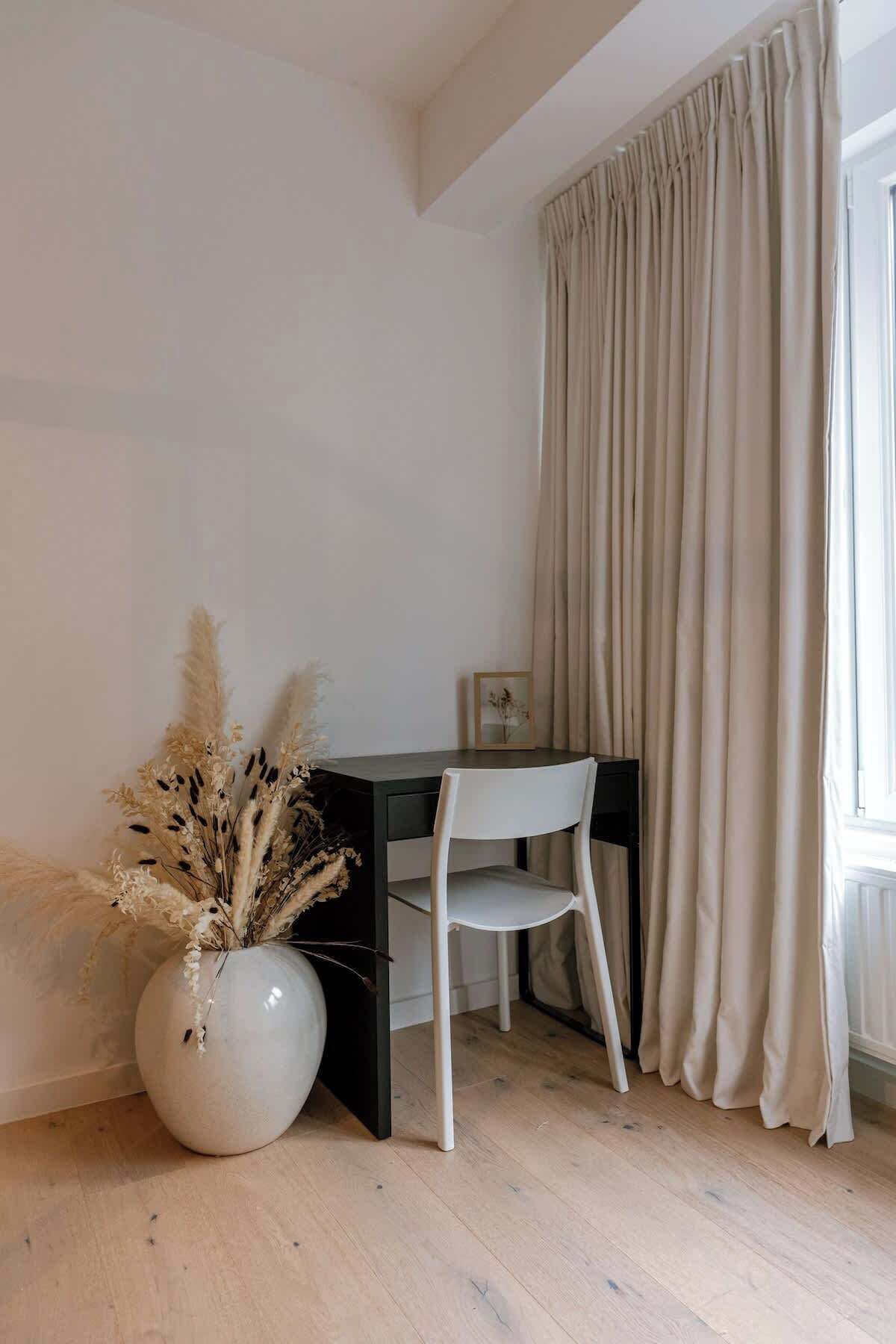 A room with a desk, chair, and a large window with curtains.