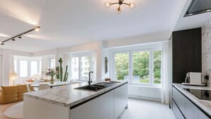 A modern kitchen with a central island, large windows, and a dining area with a round table and chairs. - Family-ready apt w/ game console - heart of Ostend (Oostende)