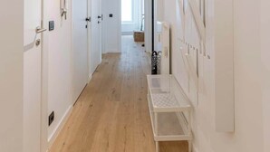 A hallway with white walls, wooden flooring, and a white bench. - Family-ready apt w/ game console - heart of Ostend (Oostende)