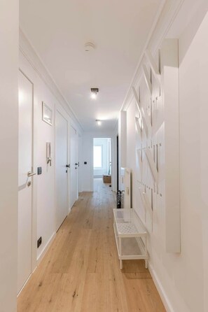 Un pasillo con paredes blancas, suelo de madera y un banco blanco.