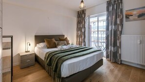 Een slaapkamer met een bed, nachtkastje, lamp en uitzicht.