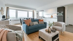 Een moderne woonkamer met een bank, salontafel en een eethoek met stoelen.