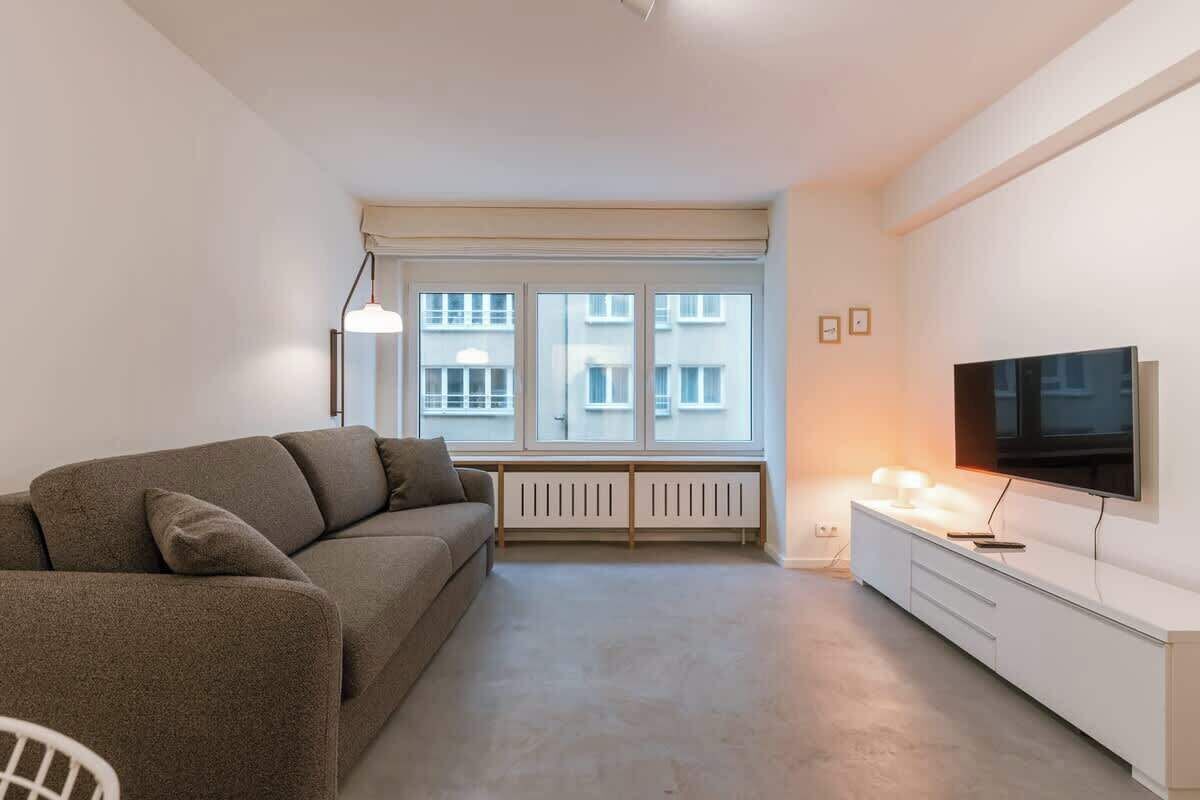 A bright, open-concept room designed for both relaxation and rest, featuring a large flat-screen TV and a comfortable sofa.