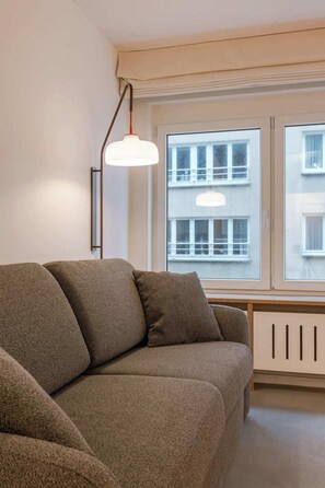 Ein Wohnzimmer mit einer Couch, einer Pendelleuchte und einem Fenster mit Blick auf Gebäude.