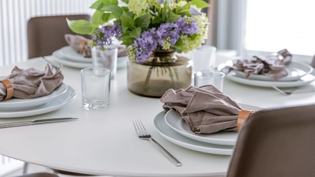 Una mesa de comedor lista con platos, cubiertos y un centro de mesa con flores.