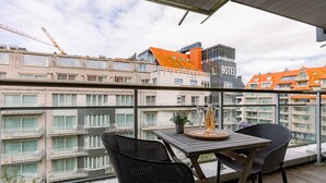 Un balcón con mesa y sillas, con vista a un paisaje urbano que incluye edificios y un hotel.