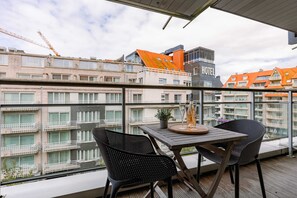 Ein Balkon mit Tisch und Stühlen, der auf einen Stadtblick mit Gebäuden und einem Hotel blickt.