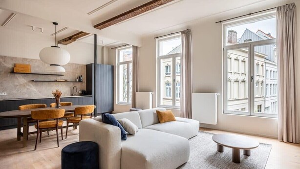 Una sala moderna con sofá, reposapiés, mesa de comedor, sillas y una lámpara colgante.
