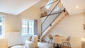 A modern living room with a staircase, a sofa, a round table, and chairs. - Duplex studio near Ghent's centre (Gent)