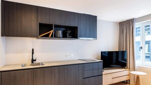 A modern kitchen with dark wood cabinets, a built-in oven, a sink, and a flat-screen TV. - Duplex studio near Ghent's centre (Gent)