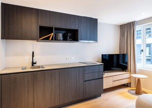 Une cuisine moderne avec des meubles en bois foncé, un four encastré, un évier et un téléviseur à écran plat.