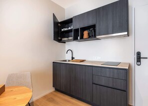 A compact kitchen with dark wood cabinets, a built-in sink, and a small dining area with a wooden table and chair. - Light-filled studio w/ workspace (Gent)
