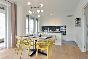 A modern kitchen with white cabinets, a central island, and a dining area with yellow chairs and a round table. - Bright coastal retreat w/ kitchen & parking (Oostende)
