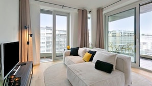 Ein modernes Wohnzimmer mit einer Couch, einem Fernseher und einem Balkon mit Blick auf Gebäude.