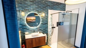 Ein Badezimmer mit rundem Spiegel, Waschbecken und einer Duschkabine.