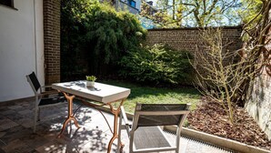 Eine Terrassengruppe mit Tisch und Stühlen, umgeben von einer Ziegelmauer und viel Grün.