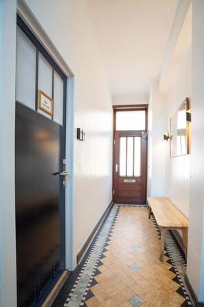 A hallway with a dark door, a wooden bench, and a tiled floor.