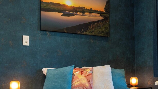Ein Schlafzimmer mit einem Bett, Kissen, einem Nachttisch, einem Wandbild und einer Nachttischlampe.