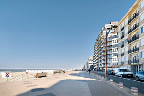 A coastal promenade with a row of multi-story buildings, a pedestrian walkway, and a beach in the background. - Cozy apartment w/ balcony & parking (Knokke-Heist)