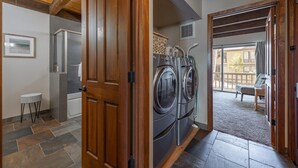A laundry room with two front-loading washers and dryers, a small table, and a bench in a covered outdoor area. - Kingswood Village 57 3 Bedroom Condo (Kings Beach)