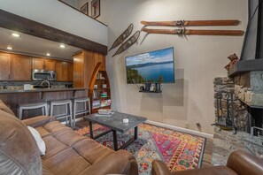 Una sala de estar con chimenea, una cocina al fondo y un ventanal con vistas panorámicas.