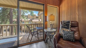 A room with a sliding glass door leading to an outdoor deck, a small round table with a lamp, and a leather chair with a cushion. - Kingswood Village 57 3 Bedroom Condo (Kings Beach)