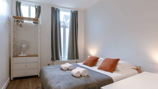 A bedroom with a bed, a bedside table, a fan, a window with curtains, and a wardrobe. - 3BR apartment w/ kitchen (Gent)
