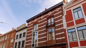 A red brick building with a white door and windows, a white van parked in front, and a cobblestone street. - 3BR apartment w/ kitchen (Gent)