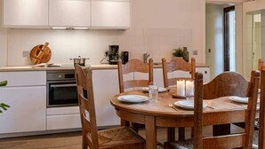 A modern kitchen with white cabinets, a wooden dining table with chairs, and a pendant light fixture. - 3BR apartment w/ kitchen (Gent)