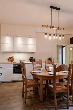 A modern kitchen with white cabinets, a wooden dining table with chairs, and a pendant light fixture.