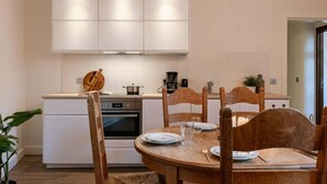 A modern kitchen with white cabinets, a wooden dining table, and a built-in oven. - 3BR apartment w/ kitchen (Gent)