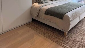 Ein Schlafzimmer mit einem Bett, einem Kleiderschrank, einem Fenster mit Vorhängen und Blick auf Gebäude.