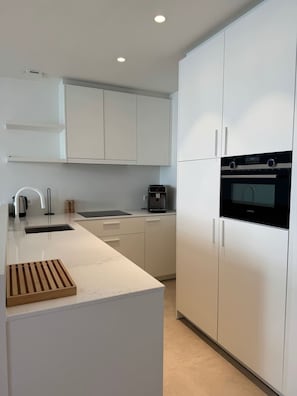 Una cocina moderna con armarios blancos, horno empotrado y cafetera.