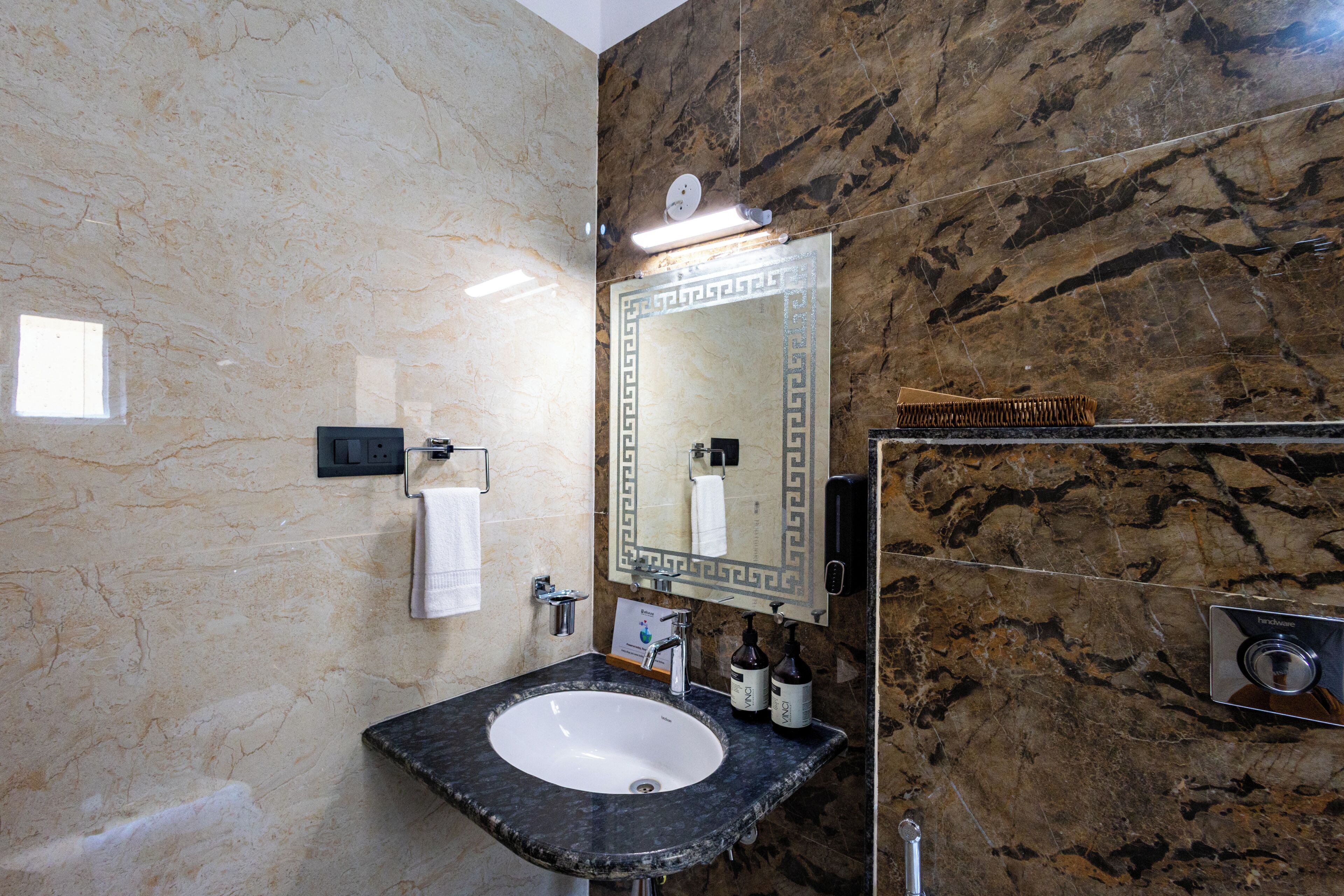 A bathroom with a marble sink, a mirror with a decorative frame, a towel rack, and a hand dryer.