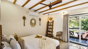 A bedroom with a bed, a ceiling fan, a wooden shelf, a chair, and a balcony with outdoor furniture. - ELIVAAS Casa llios Stuning Getaway Villa (Udaipur)