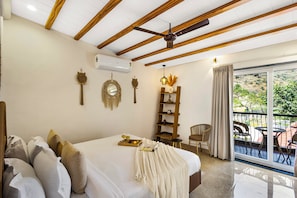 Un dormitorio con cama, ventilador de techo, estante de madera, una silla y un balcón con mobiliario exterior.