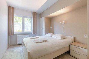 Une chambre à coucher avec un lit, des tables de chevet, un radiateur et une fenêtre avec des rideaux.