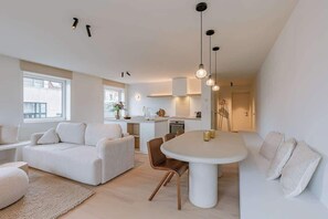 Ein modernes Interieur mit einer weißen Sofagarnitur, einem Esstisch und Pendelleuchten.