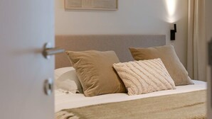 Ein Schlafzimmer mit Bett, Kissen, Decke, Wandbild und Nachttisch mit Lampe.