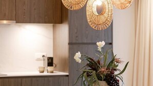 Eine moderne Küche mit Holzausstattung, einem Esstisch mit Stühlen und drei hängenden Korbstuhlpendelleuchten.