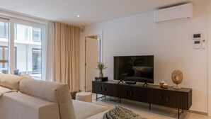 Ein modernes Wohnzimmer mit großem Flachbildfernseher, einer Couch, einem Couchtisch und einem Beistelltisch mit Pflanze.